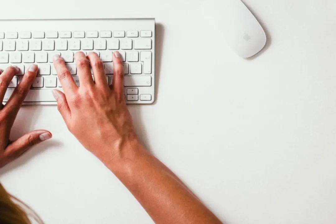 Hands on a white keyboard next to a mouse on a desk