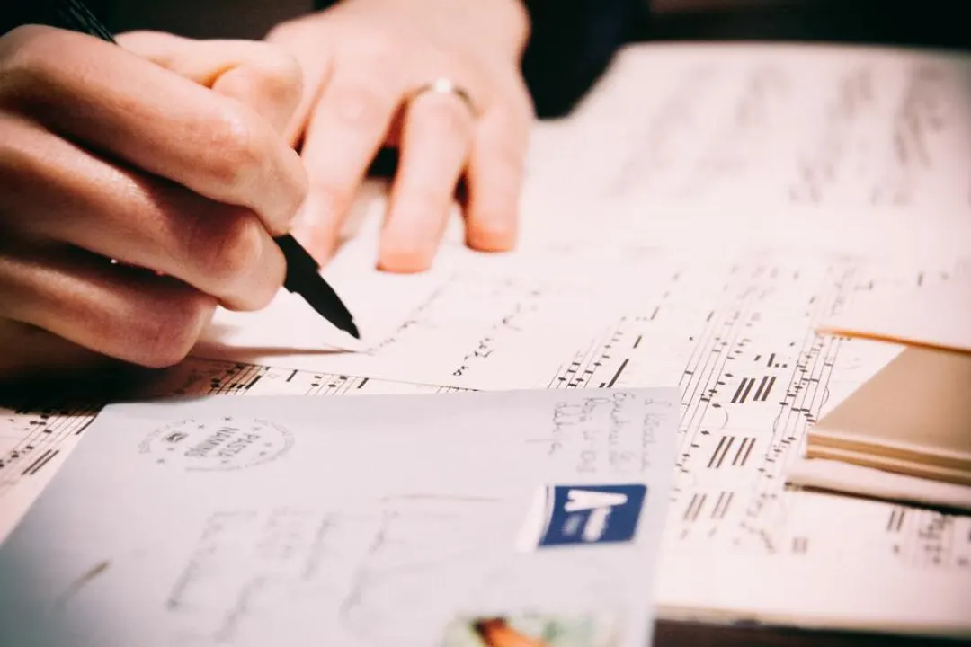 A hand writing in pen on a sheet of paper, next to envelopes and writing paper