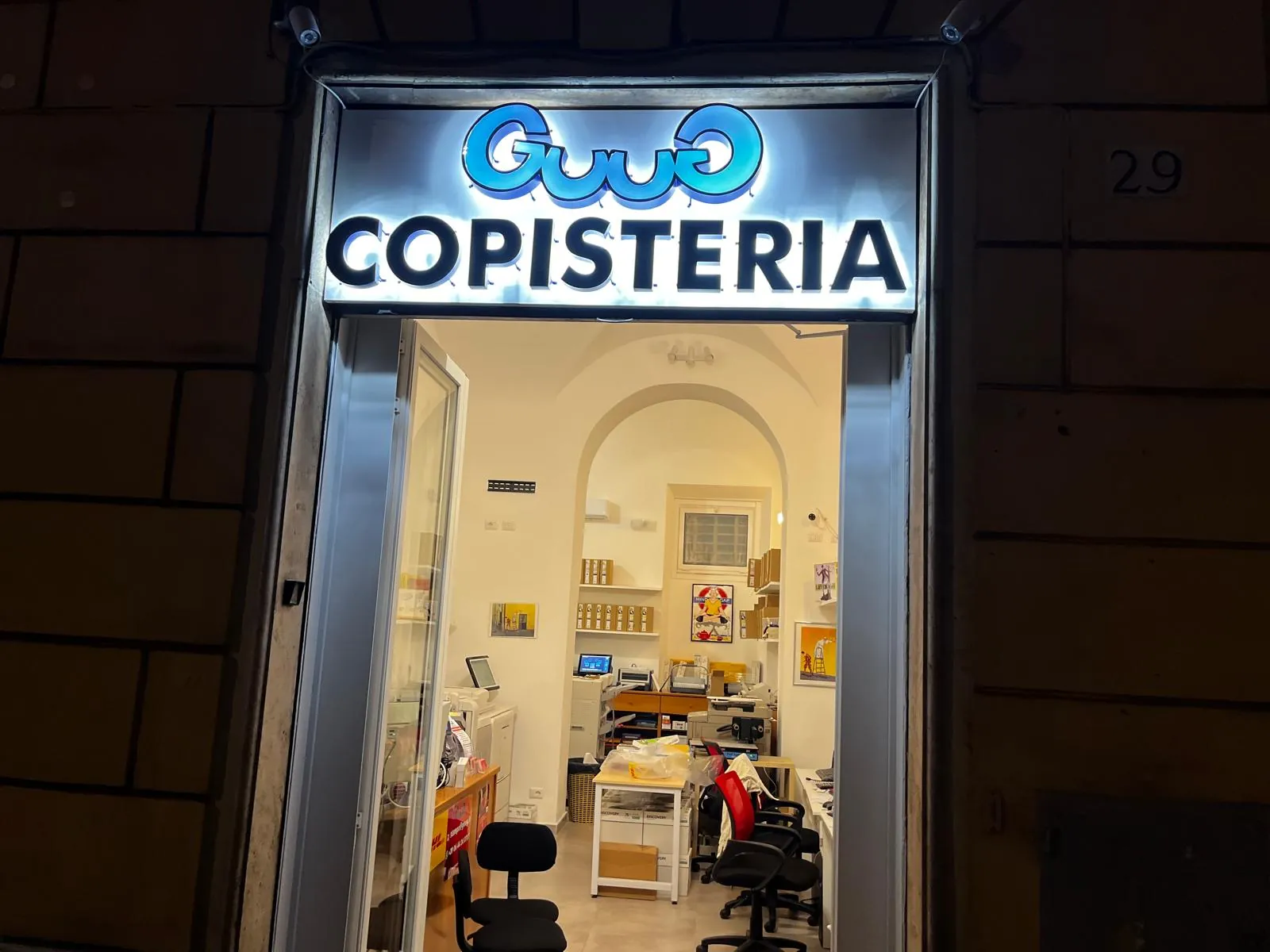 The GUUG copy shop at Via di Porta Castello 29 in Rome lit up in the evening, blue sign glowing