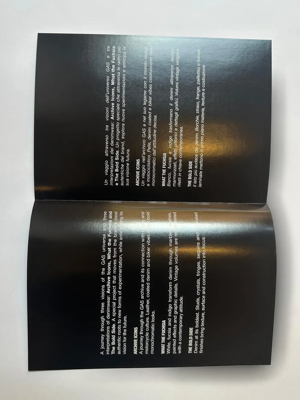 GAS × Elite brochure, open: inside spread on black coated paper with white bilingual text about the denim collections, printed by GUUG
