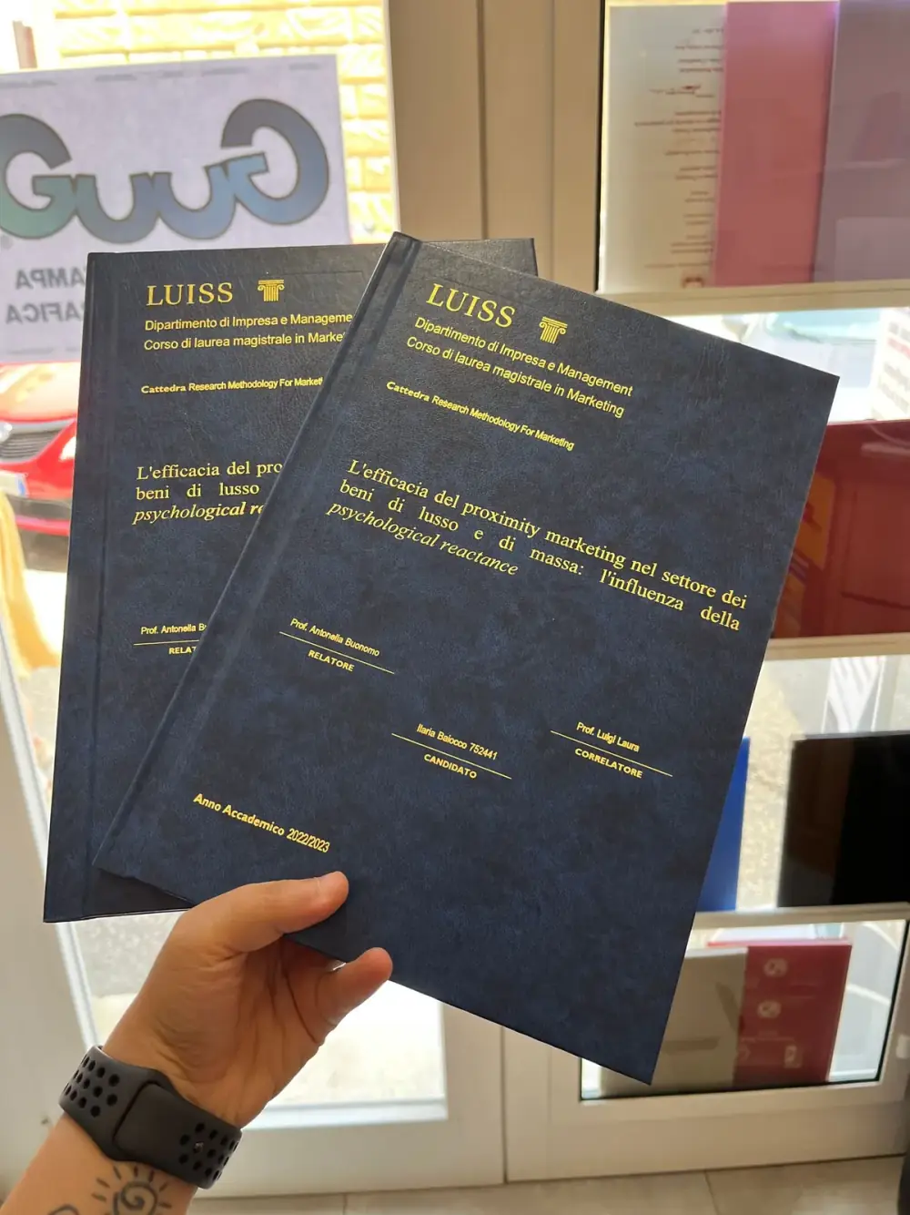Tesi LUISS Marketing rilegata da GUUG, copertina blu notte istituzionale con foil oro, due copie in primo piano nel negozio di Roma Prati